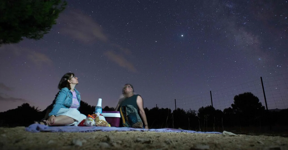 night sky meteor shower with people watching from meadow in Czech Republic