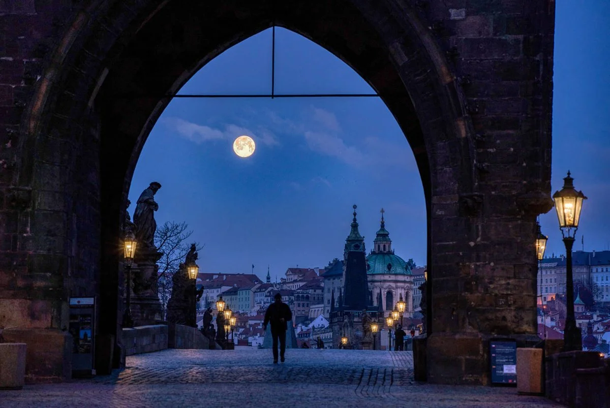 person watching large full moon over prague from charles bridge night